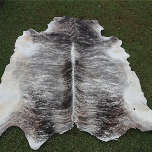 Pode incluir: Um tapete de pele de vaca com um padr&atilde;o branco e cinza. A pele est&aacute; estendida sobre uma superf&iacute;cie de grama verde.