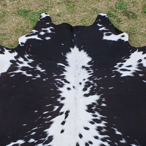 May include: Black and white cowhide rug with a spotted pattern. The hide is soft and supple, with a natural sheen.