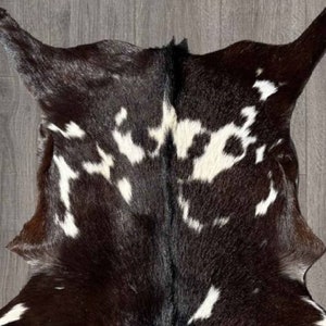 Puede incluir: Una alfombra de piel de vaca negra y blanca con un patr&oacute;n natural moteado. La piel es suave y flexible, con una sensaci&oacute;n de lujo.