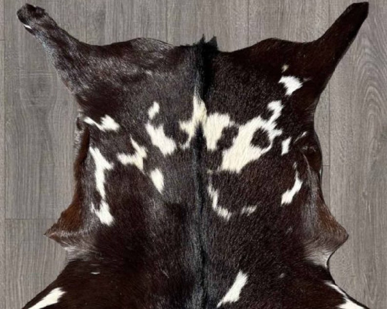 Puede incluir: Una alfombra de piel de vaca negra y blanca con un patr&oacute;n natural moteado. La piel es suave y flexible, con una sensaci&oacute;n de lujo.