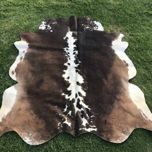 Op de afbeelding: Een bruin en wit koeienhuidkleed met een natuurlijke, onregelmatige vorm. De huid heeft een kenmerkend patroon van bruine en witte vlekken.