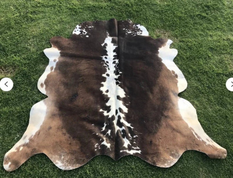 Op de afbeelding: Een bruin en wit koeienhuidkleed met een natuurlijke, onregelmatige vorm. De huid heeft een kenmerkend patroon van bruine en witte vlekken.