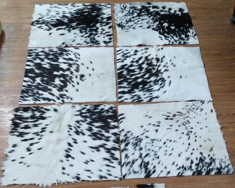 Puede incluir: Un conjunto de piezas rectangulares de piel de vaca, cada una con un patr&oacute;n &uacute;nico de manchas negras sobre fondo blanco. Las pieles est&aacute;n dispuestas sobre una superficie de madera, mostrando sus texturas y variaciones naturales.