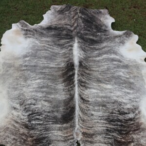 Pode incluir: Um tapete de pele de vaca com um padr&atilde;o branco e cinza. A pele est&aacute; dobrada ao meio, mostrando o gr&atilde;o natural do couro.