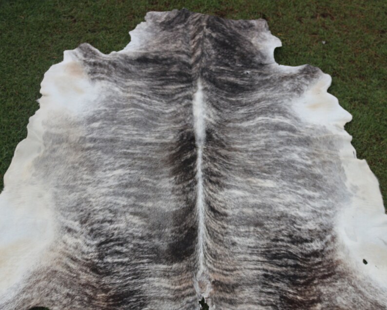 Pode incluir: Um tapete de pele de vaca com um padr&atilde;o branco e cinza. A pele est&aacute; dobrada ao meio, mostrando o gr&atilde;o natural do couro.