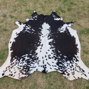 Op de afbeelding: Zwart-witte koeienhuidkleed met een gevlekt patroon. Het kleed is gemaakt van natuurlijk koeienhuid en heeft een zachte, soepele textuur.
