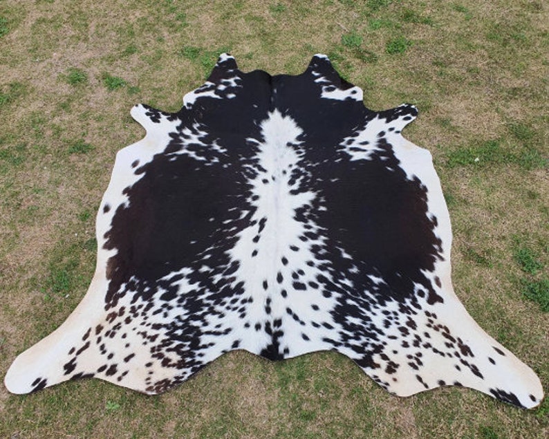Op de afbeelding: Zwart-witte koeienhuidkleed met een gevlekt patroon. Het kleed is gemaakt van natuurlijk koeienhuid en heeft een zachte, soepele textuur.