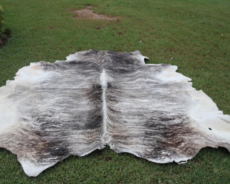 Pode incluir: Um tapete de pele de vaca com um padr&atilde;o branco e cinza. O tapete est&aacute; colocado sobre uma superf&iacute;cie de grama verde.