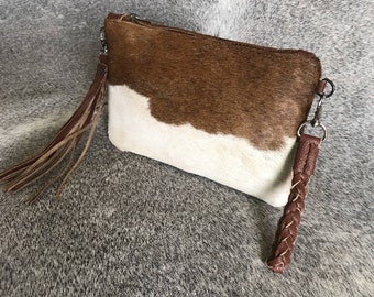Może przedstawiać: Brązowa i biała torebka typu clutch ze skóry krowiej z plecionym paskiem skórzanym i frędzlem.