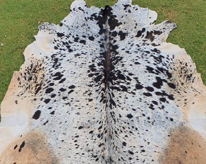 May include: A cowhide rug with a white, black, and brown spotted pattern. The hide is folded in half, showing the natural grain of the leather.