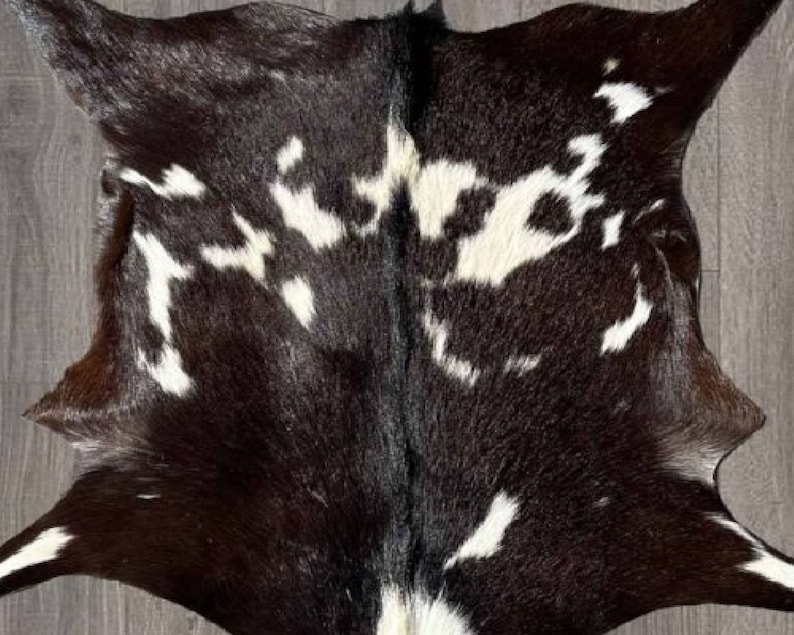 Puede incluir: Una alfombra de piel de vaca negra y blanca con una textura natural y suave. La piel tiene un patr&oacute;n &uacute;nico de manchas blancas sobre un fondo negro.