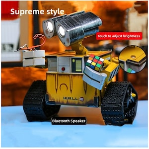 Könnte beinhalten: Ein gelbes und schwarzes Roboter-Spielzeug mit einem Rubik's Cube in der Hand. Der Roboter hat ein Licht auf seinem Kopf und sagt "WALL-E" auf seiner Brust. Der Roboter ist ein Bluetooth-Lautsprecher.