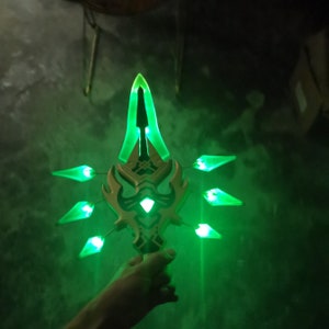 May include: A green and gold plastic toy sword with a glowing green light. The sword has a pointed tip and a handle with a decorative design.