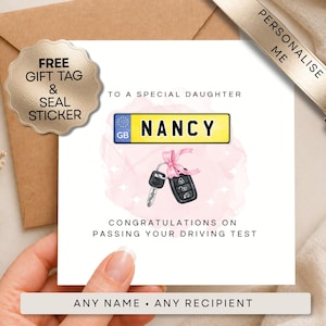 May include: A white card with the text "TO A SPECIAL DAUGHTER" and "CONGRATULATIONS ON PASSING YOUR DRIVING TEST". The card features a license plate with the name "NANCY" and a car key with a pink bow.