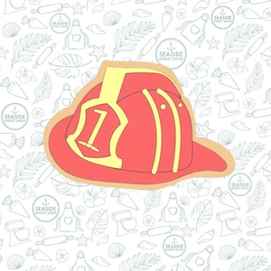 May include: A red and yellow firefighter helmet cookie decorated with a number one on the front. The cookie is on a white background with a pattern of seashells, stars, and other beach-themed designs.