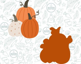 May include: Three pumpkins on a white background with a pattern of seashells, palm leaves, and anchors. The pumpkins are orange and white. The largest pumpkin is in the back and the smallest pumpkin is in the front. The pumpkins are all in focus.