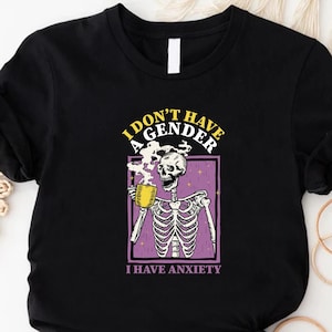 May include: Black t-shirt with a skeleton graphic holding a yellow mug. The graphic includes the text "I DON'T HAVE A GENDER, I HAVE ANXIETY" in yellow and purple. The skeleton is inside a purple rectangle.
