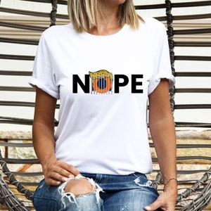 May include: White t-shirt with the word "NOPE" printed in black letters. A cartoon image of a person's hair is inside the "O" of the word "NOPE".