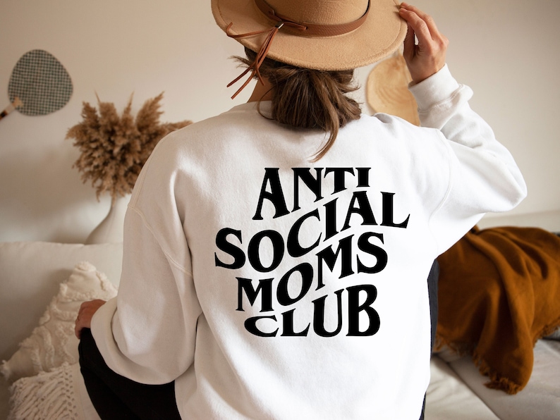 Puede incluir: Sudadera blanca con texto negro que dice "Anti Social Moms Club" en una fuente retro.