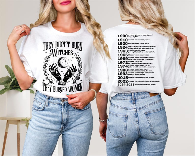 以下が含まれることがあります： 「THEY DIDN'T BURN WITCHES THEY BURNED WOMEN」の黒い文字がプリントされた白いTシャツ。 月と手のデザイン。 Tシャツの背面には、女性の権利に関する重要な日付が記載されています。