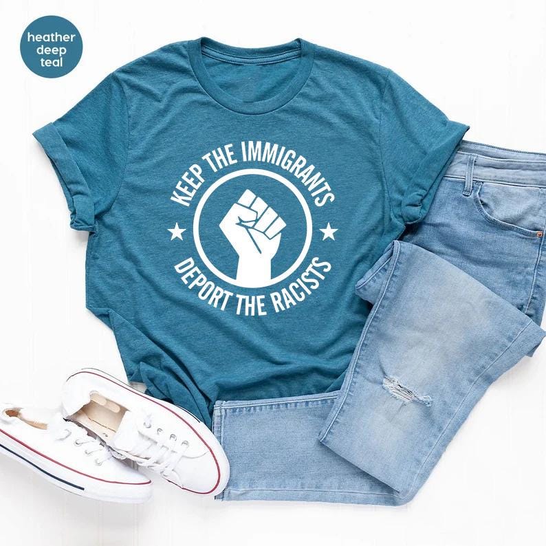 K&ouml;nnte beinhalten: Ein tealfarbenes T-Shirt mit dem Text "KEEP THE IMMIGRANTS DEPORT THE RACISTS" in einem wei&szlig;en Kreisdesign mit einer erhobenen Faust. Das Shirt wird mit hellblauen Jeans und wei&szlig;en Turnschuhen kombiniert.