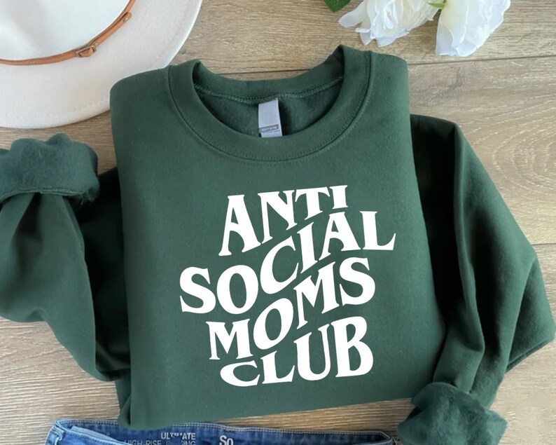 Puede incluir: Una sudadera verde oscuro con texto blanco que dice "Anti Social Moms Club" en una fuente retro.