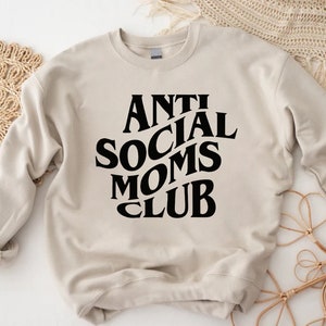 Puede incluir: Una sudadera beige con texto negro que dice "Anti Social Moms Club".