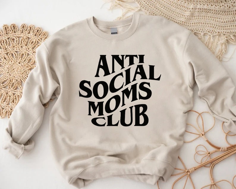 Puede incluir: Una sudadera beige con texto negro que dice "Anti Social Moms Club".