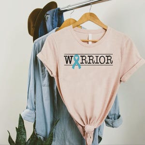 a pink shirt with a blue ribbon on the front and a blue ribbon on the