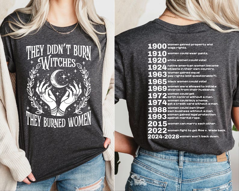 以下が含まれることがあります： 「THEY DIDN'T BURN WITCHES THEY BURNED WOMEN」の白文字がプリントされた濃いグレーのTシャツ。デザインには月、星、手が含まれています。背面には、1900年から2028年までの女性の権利の節目が記載されています。