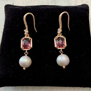 Peut inclure: Une paire de boucles d'oreilles pendantes en or avec une pierre précieuse rectangulaire à facettes rose foncé suspendue à un crochet incurvé, un petit accent en pierre claire et une perle blanche ronde suspendue au bas de chaque pièce.