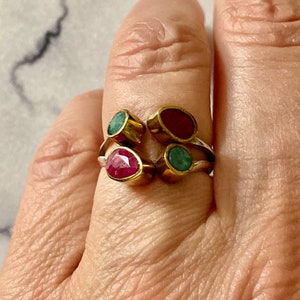 Peut inclure: Une bague en or avec trois pierres précieuses. La bague a deux pierres précieuses vertes et une pierre précieuse rouge.