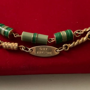 Peut inclure: Un collier en chaîne dorée avec des perles rayées vertes et blanches et une étiquette ovale dorée qui indique "GUY LAROCHE".