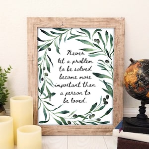 Könnte beinhalten: Ein gerahmter Druck mit weißem Hintergrund und grünen Aquarellblättern und schwarzen Oliven. Der Druck zeigt das Zitat "Lass niemals ein Problem, das gelöst werden muss, wichtiger werden als ein Mensch, der geliebt werden soll."