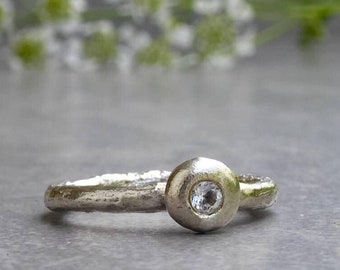 May include: A silver ring with a textured band and a round bezel set with a clear gemstone.