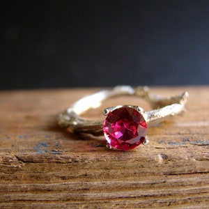 May include: A silver ring with a branch-like design and a bright pink gemstone.
