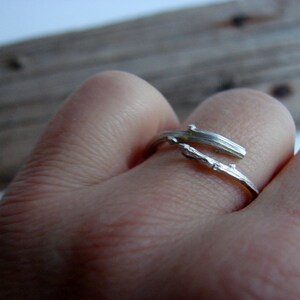 May include: A silver ring shaped like a twig, worn on a finger.