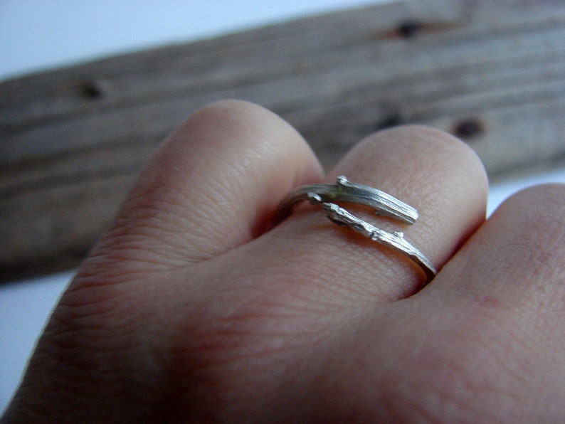 May include: A silver ring shaped like a twig, worn on a finger.