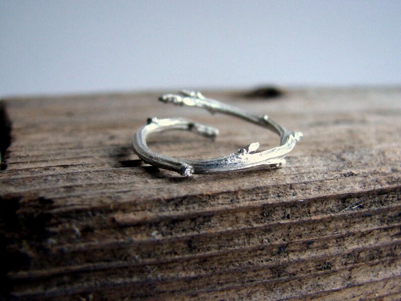 May include: A silver ring shaped like two intertwined branches with small leaf details.