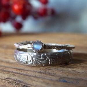 Könnte beinhalten: Zwei silberne Ringe mit einem Mondstein, der in den oberen Ring eingefasst ist. Der untere Ring hat ein florales Design und der obere Ring ist ein dünnes Band mit einem Zweigdesign.