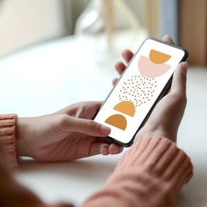 以下が含まれることがあります： ピンクとオレンジの半円が積み重ねられたデザインが施された白い背景のスマートフォンを人が持っています。デザインには茶色の水玉模様が施されています。