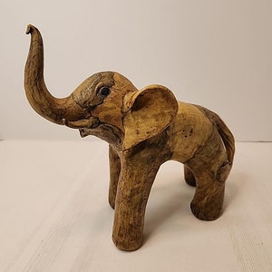 Può includere: Una statuetta di elefante in legno con la proboscide alzata e una finitura testurizzata marrone e beige.