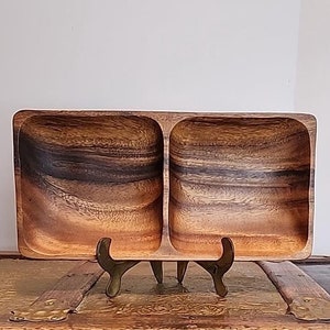May include: A wooden serving bowl with two compartments. The bowl is made of dark wood with a natural grain pattern. It is sitting on a gold metal stand.