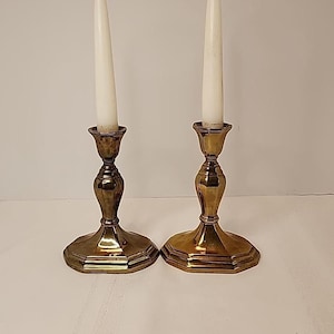 Puede incluir: Un par de candelabros de metal dorado con velas blancas. Los candelabros tienen un diseño acanalado y una base redonda.