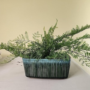以下が含まれることがあります： 緑色のセラミック製のプランターにシダ植物が入っています。プランターはテクスチャのあるストライプ模様になっています。