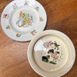 May include: A white ceramic plate with a blue rim featuring a central illustration of a child with a pumpkin and smaller vignettes around the edge, alongside a cream-coloured bowl with a central illustration of children and a black sheep.