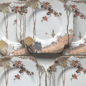 Puede incluir: Juego de cinco platos cuadrados de cerámica con fondo blanco y un delicado diseño floral en tonos marrones, naranjas y amarillos. Los platos presentan una escena de paisaje estilizada con árboles y un velero.