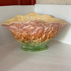 Könnte beinhalten: Eine dekorative Keramikschale mit floralem Design. Die Schale hat einen gewellten Rand und ist in Pfirsich-, Orange- und Grüntönen bemalt. Die Schale ist etwa 30 cm breit und 15 cm hoch.