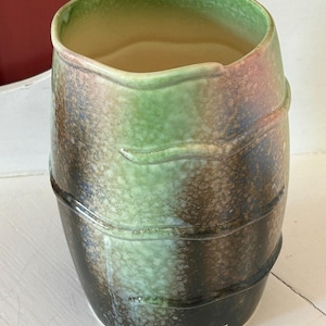 May include: A ceramic vase with a cylindrical form and a gently widening top. The vase displays a colour gradient of green, brown, and black, with a textured finish. Two horizontal bands encircle the vase, providing a decorative feature.
