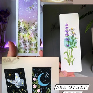 May include: Four watercolor bookmarks featuring different nature scenes. The first bookmark shows two dragonflies flying over a field of flowers. The second bookmark shows a field of lavender and daisies. The third bookmark shows a butterfly flying over a field of flowers with a crescent moon in the background. The fourth bookmark shows a field of flowers with a crescent moon in the background. The text "See other of my creations" is visible in the bottom right corner of the image.